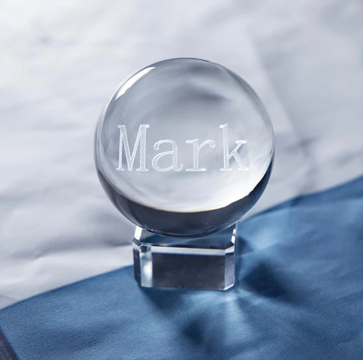 Clear crystal ball with 'Mark' engraved on it, placed on a blue fabric background