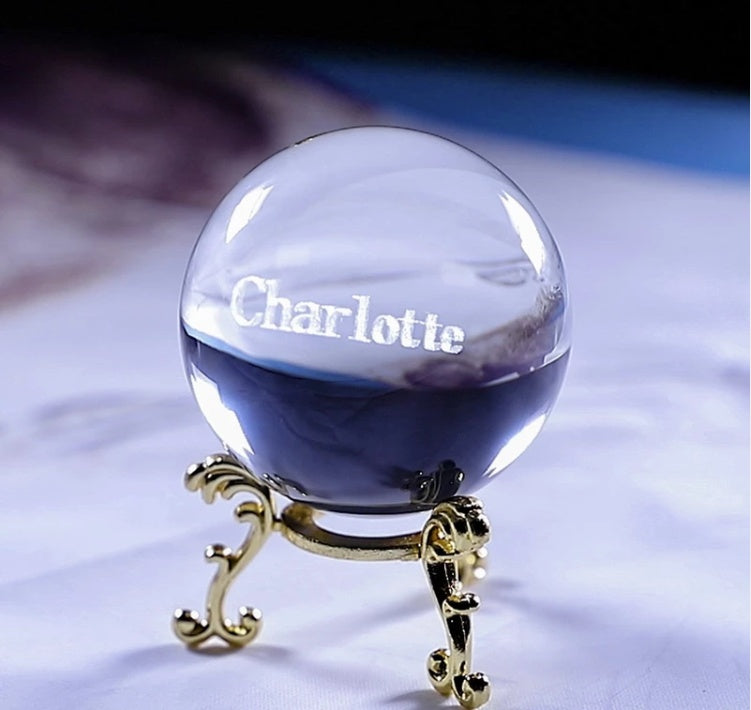 Clear crystal ball with 'Charlotte' engraved on it, placed on a decorative stand.