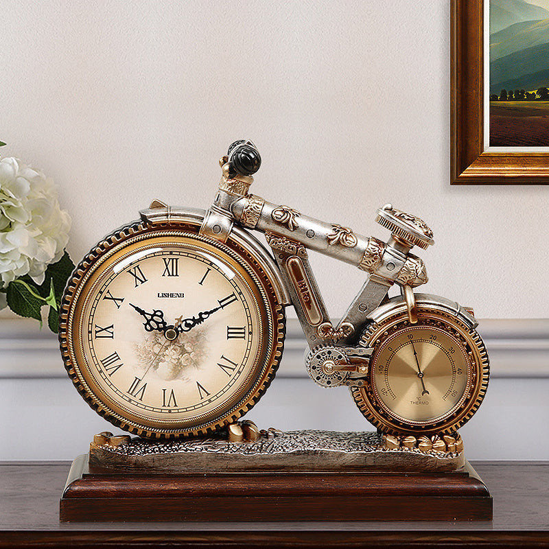 Decorative clock shaped like a motorcycle on a wooden surface with a floral arrangement and framed picture in the background.