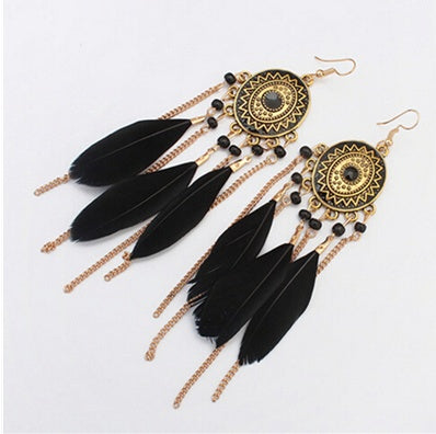 Pair of black feather earrings with gold chains and decorative elements on a white background