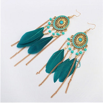 Pair of gold and teil feather earrings with gold chains and decorative elements on a white background