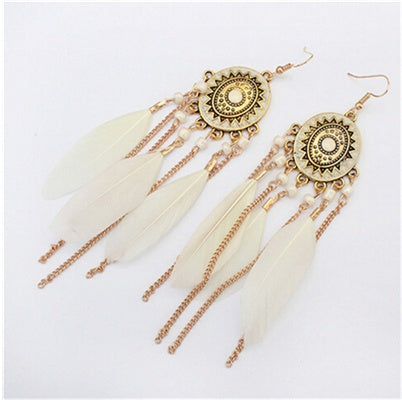 Gold earrings with decorative elements and feathers on a white background