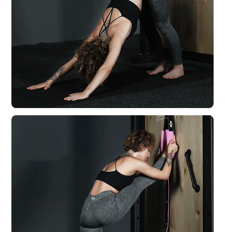 Woman performing a yoga pose on a black mat with a wooden wall in the background.