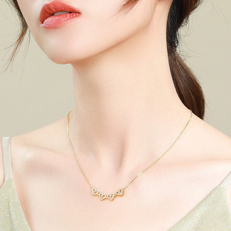 Gold necklace with heart-shaped pendants worn by a model on a neutral background