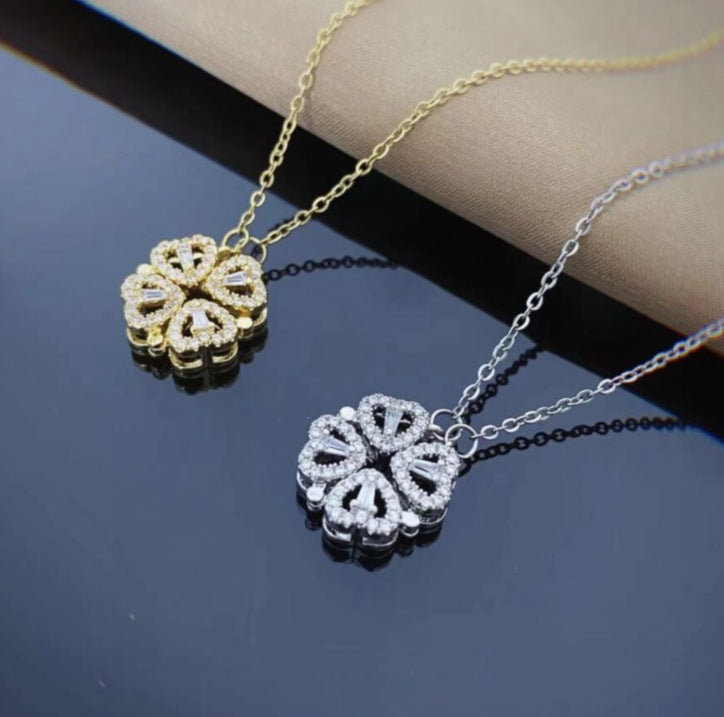 Two floral pendant necklaces, one gold and one silver, on a reflective surface.
