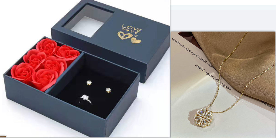 Blue jewelry box with red rose-shaped boxes and earrings, next to a necklace with a heart pendant on a beige surface.