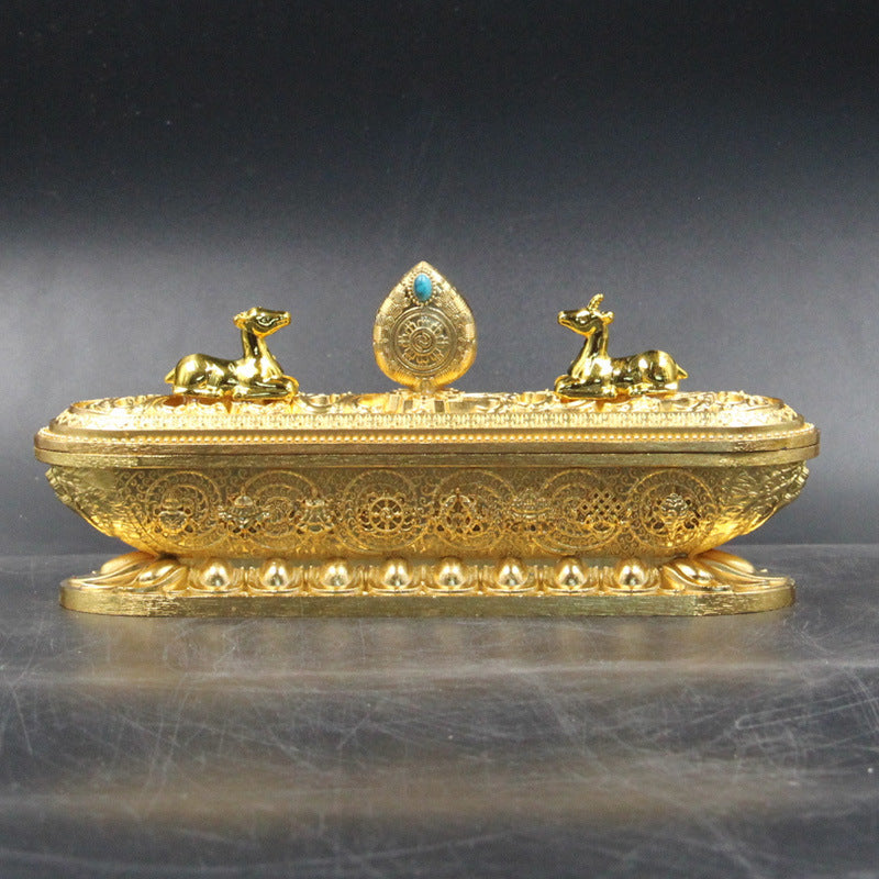 Decorative gold box with intricate designs and two small figures on a dark background