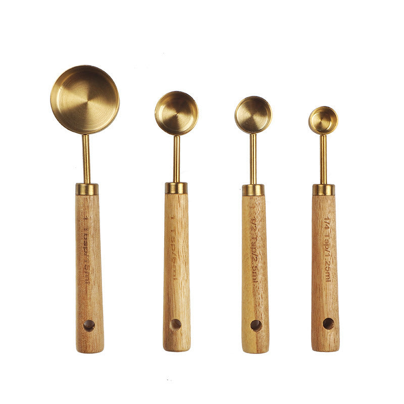 Set of four brass measuring spoons with wooden handles on a white background
