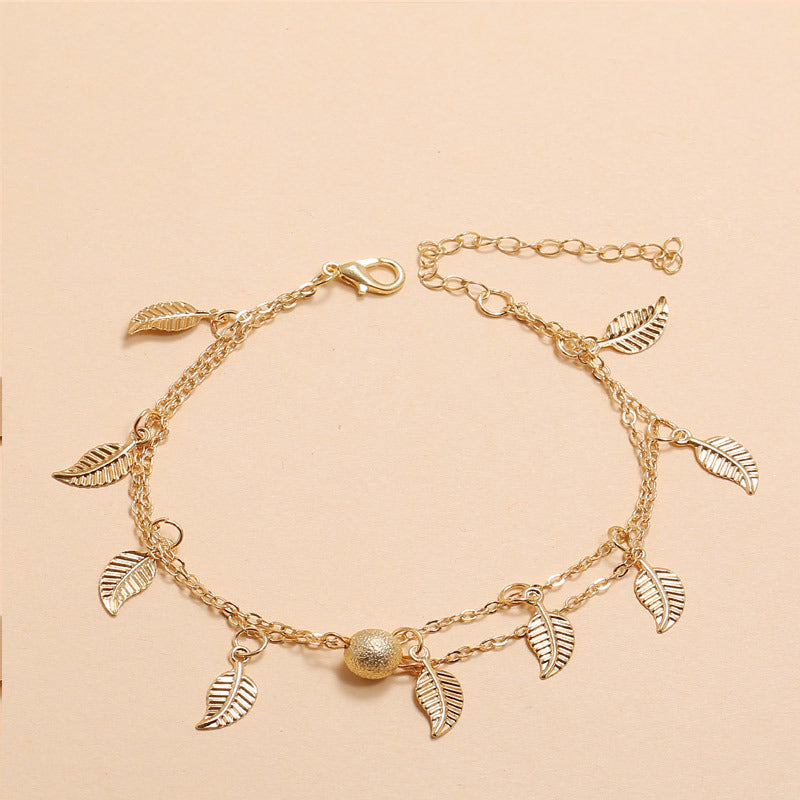 Gold anklet with leaf charms on a beige background