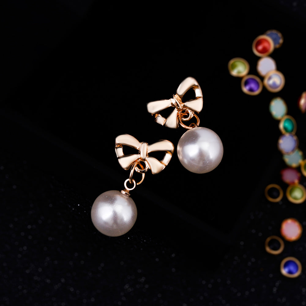 Pearl earrings with gold bow accents on a black background