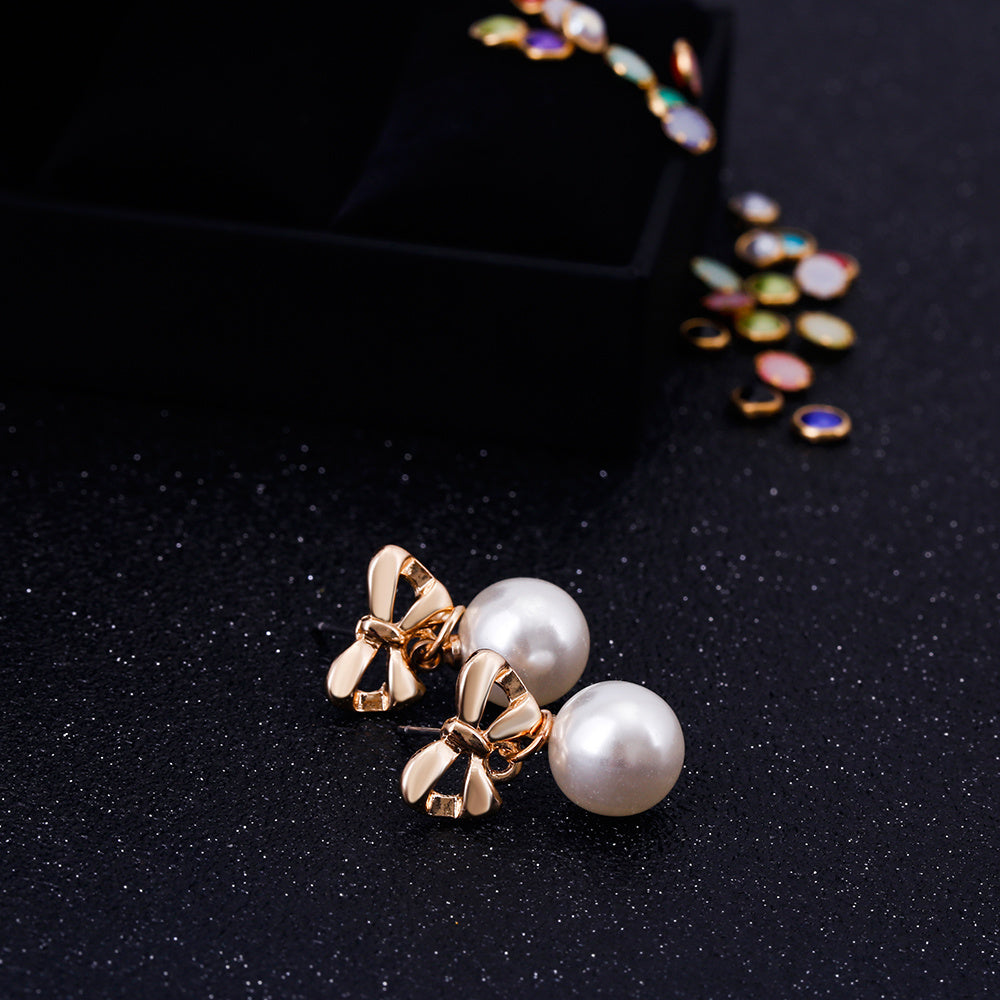 Pearl earrings with gold bow accents on a black background