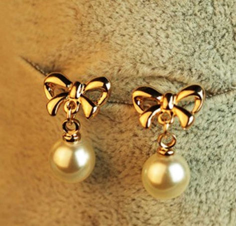 Gold bow earrings with pearl drops on a textured surface