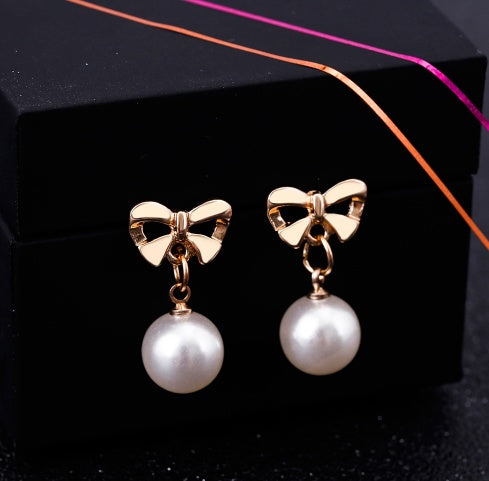 Gold bow earrings with pearl drops on a black background