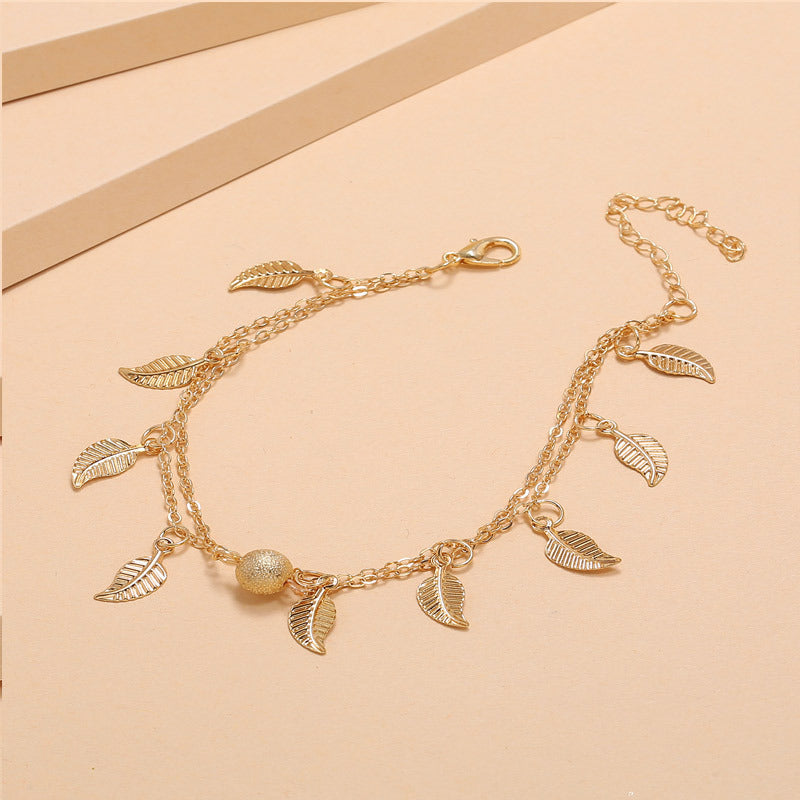 Gold bracelet with leaf charms on a beige background