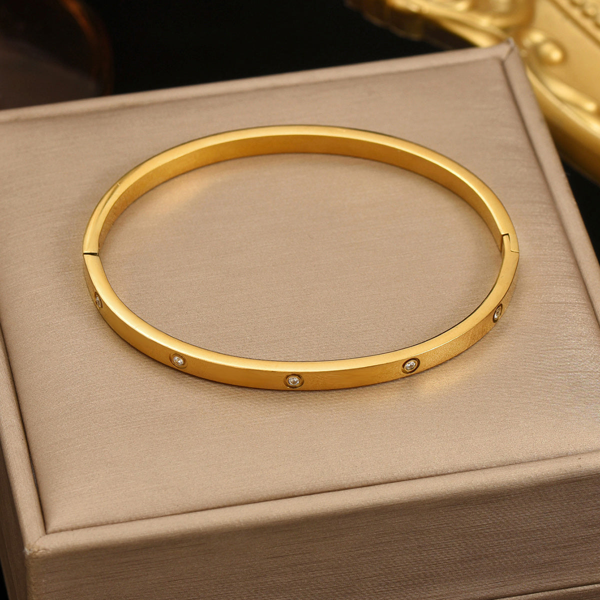 Gold bracelet with small stones on a beige jewelry box