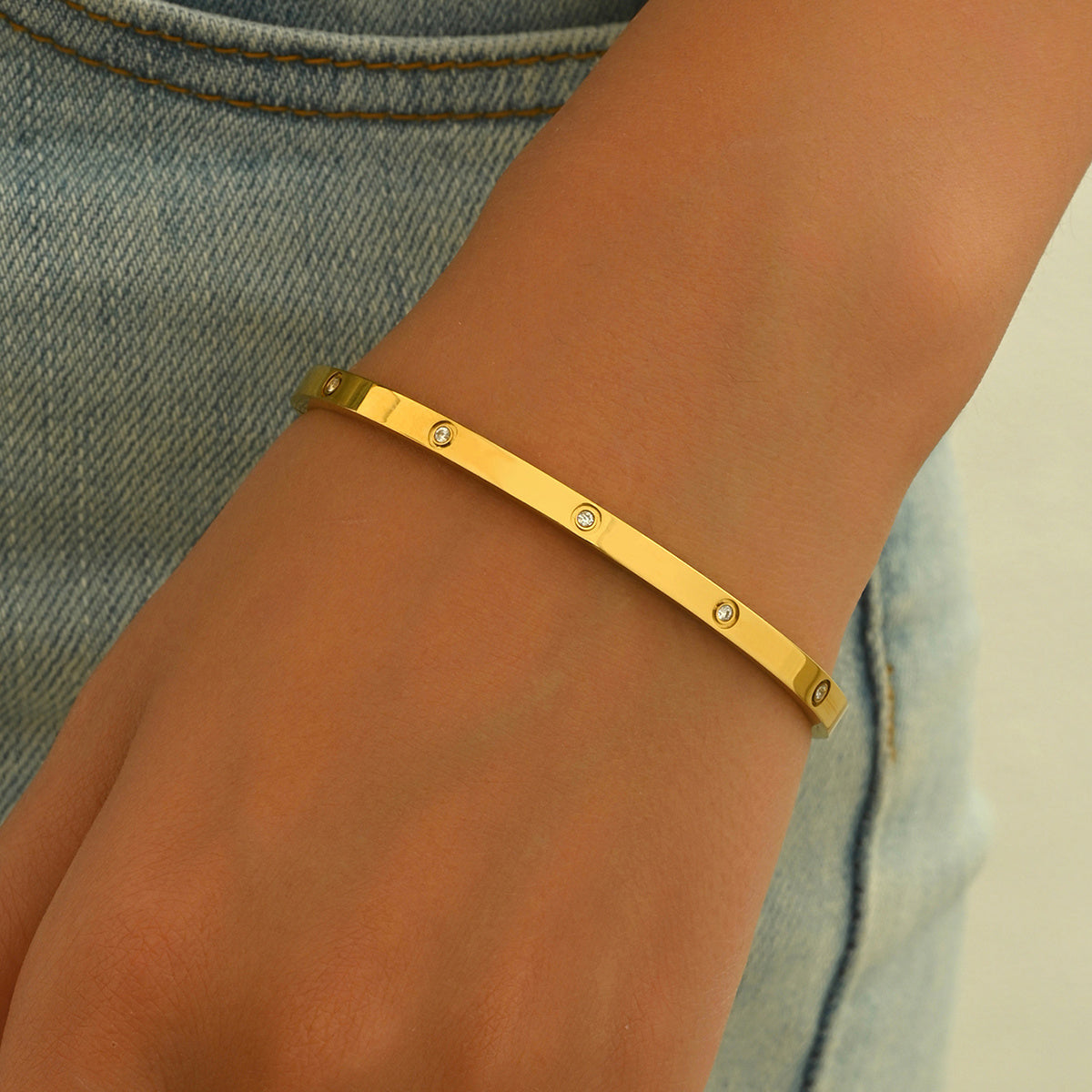 Gold bracelet with small stones on a wrist against a denim background
