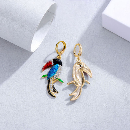 Gold earrings shaped like a toucan and a dolphin on a light gray background