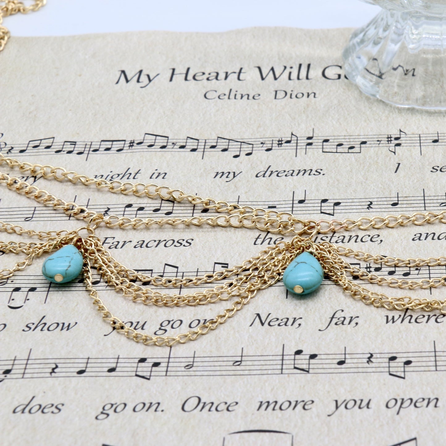 Gold chain necklace with turquoise beads on sheet music