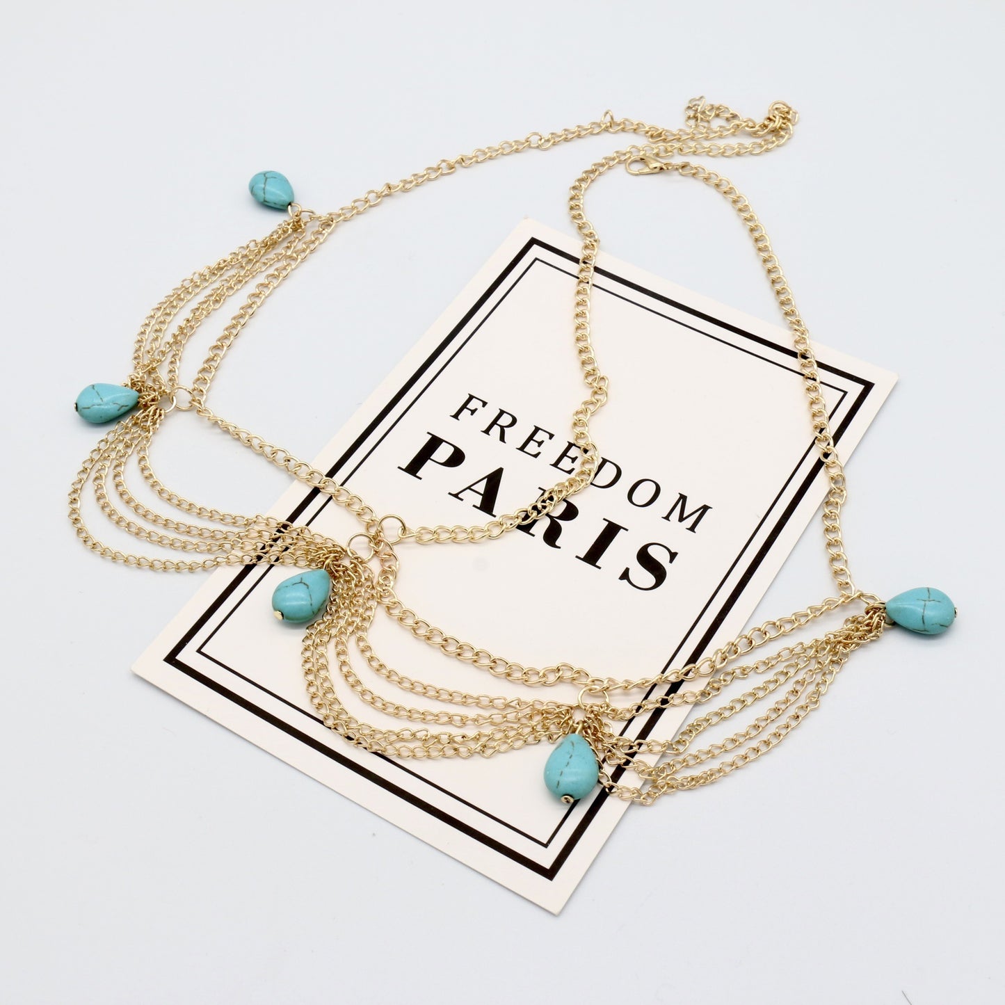 Gold necklace with turquoise beads on a 'Freedom Paris' card