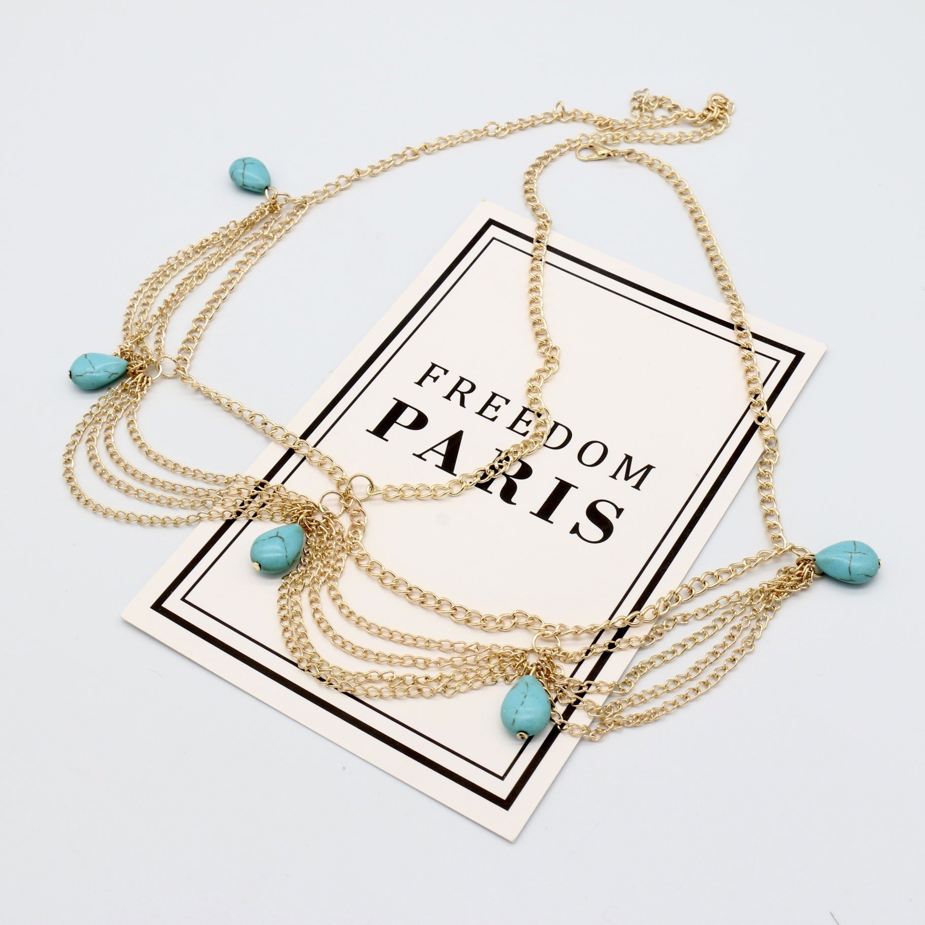 Gold necklace with turquoise beads on a 'Freedom Paris' card