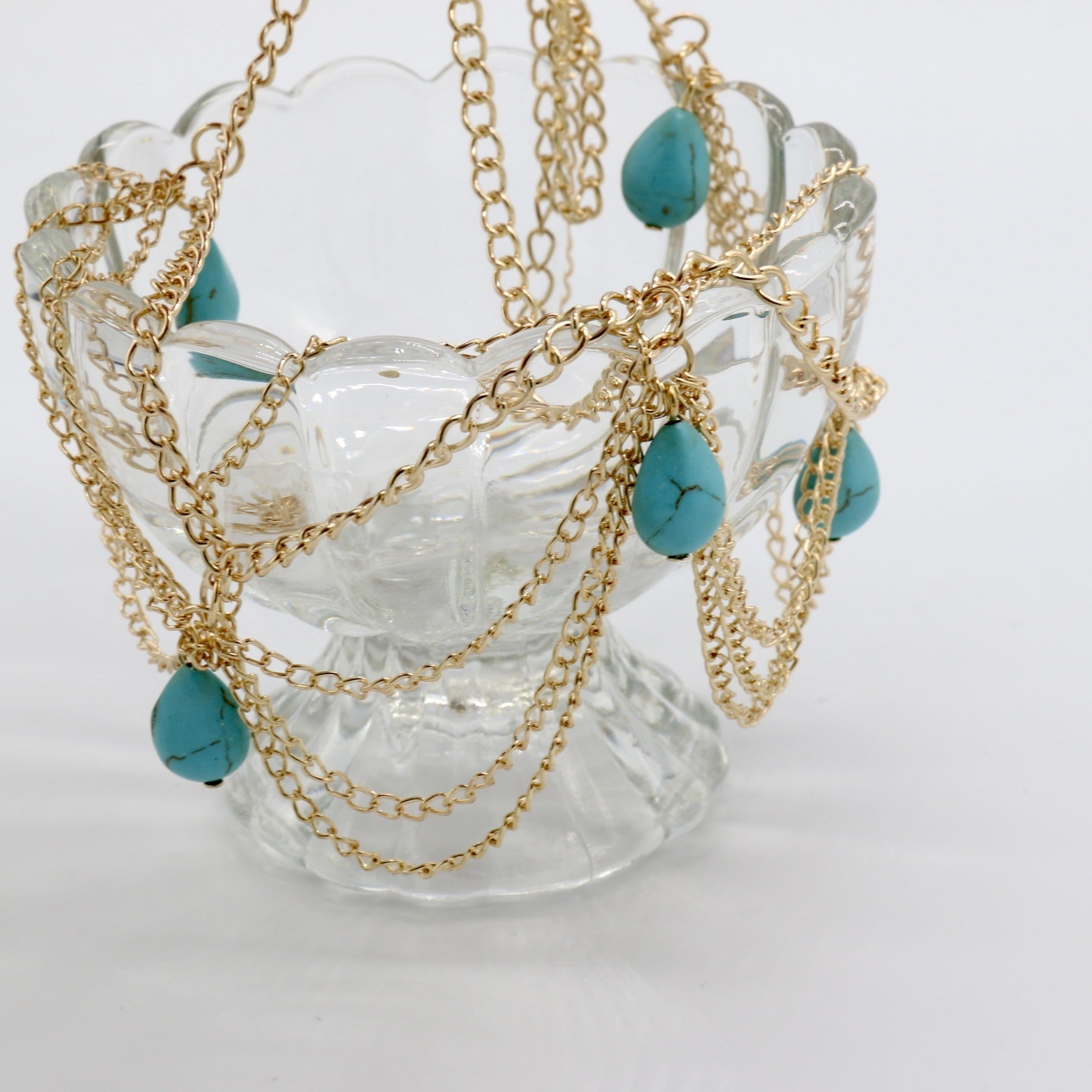 Gold chain necklace with turquoise beads on a decorative glass stand.