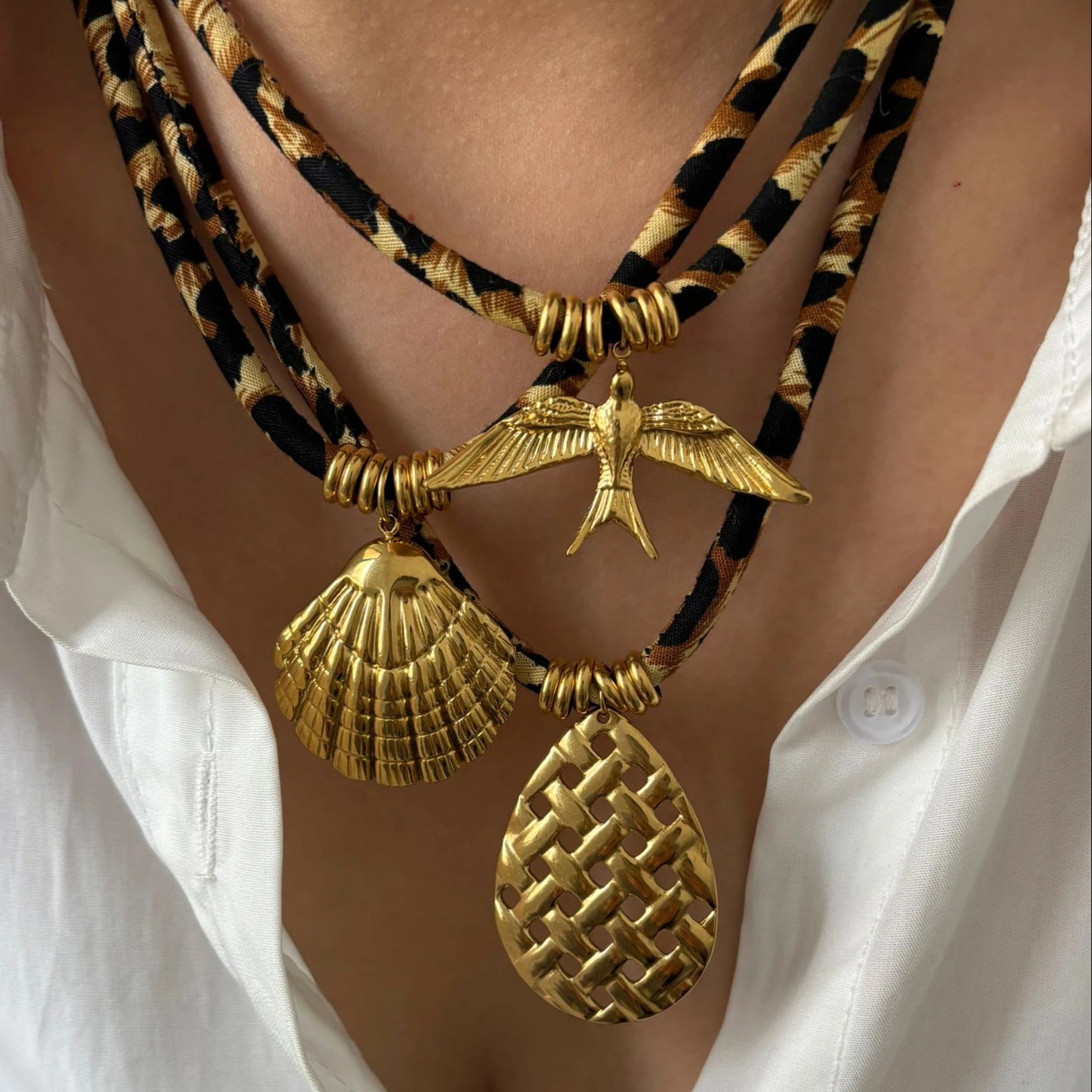 Gold necklaces with shell and bird pendants on a person wearing a white shirt.