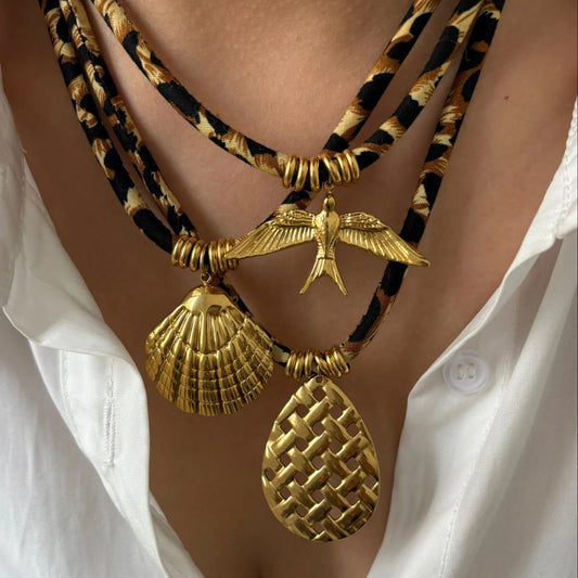 Gold necklaces with shell and bird pendants on a person wearing a white shirt.