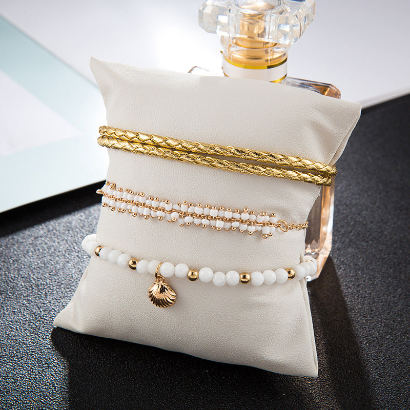 Set of gold and pearl bracelets on a white pillow with a perfume bottle in the background.
