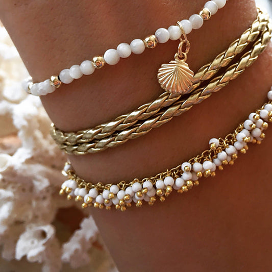 Close-up of multiple bracelets on a wrist with a shell charm against a soft background