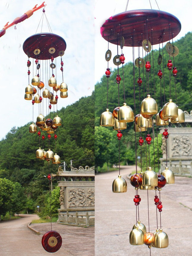 Decorative wind chime with gold bells and red beads in a natural setting.