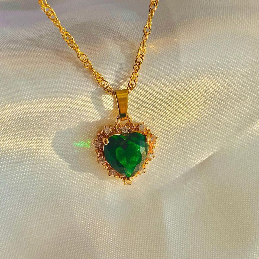 Gold necklace with a green heart-shaped pendant on a light fabric background