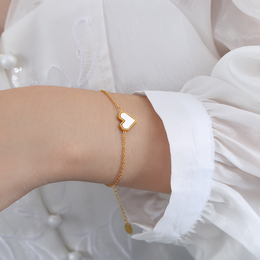 Gold bracelet with a heart charm on a wrist against a white background
