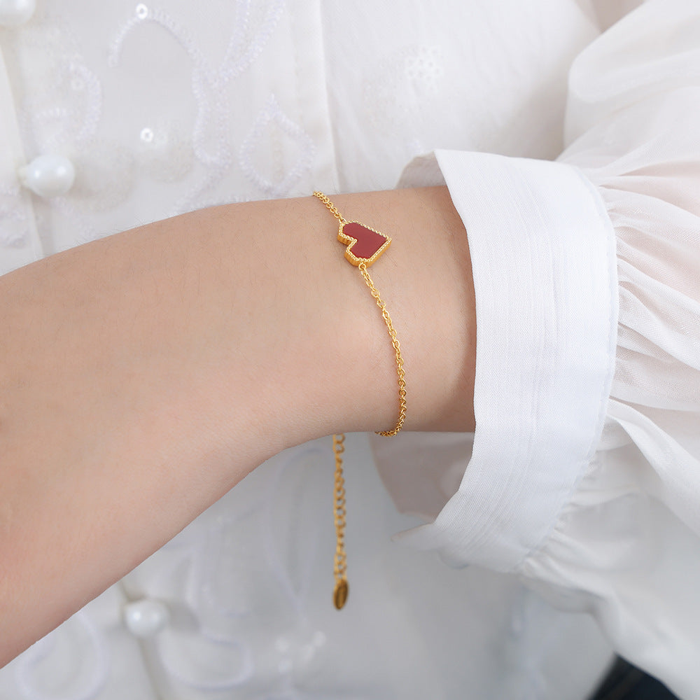 Gold bracelet with a red heart charm on a person's wrist against a white background