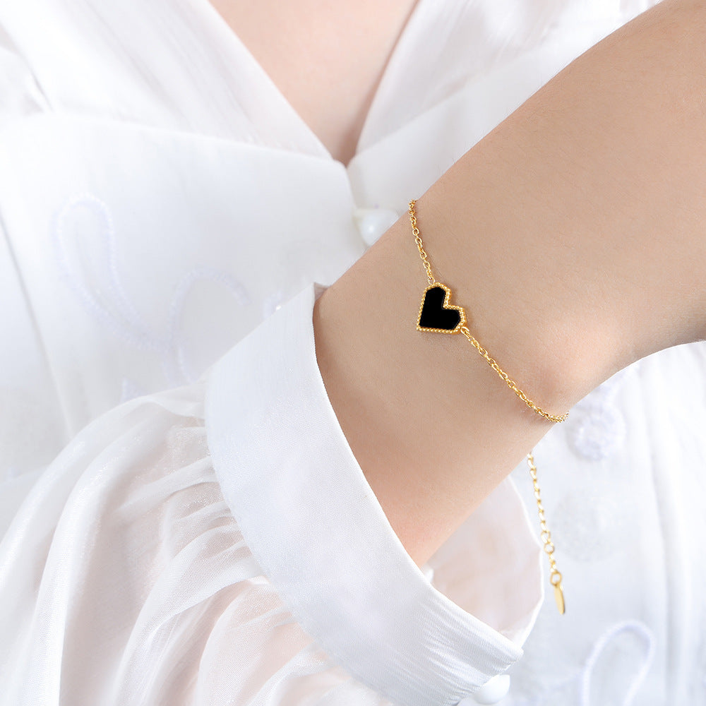 Gold bracelet with a black heart charm on a white background