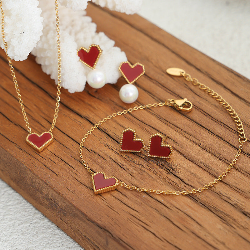 Gold heart-shaped jewelry set with red accents on a wooden surface