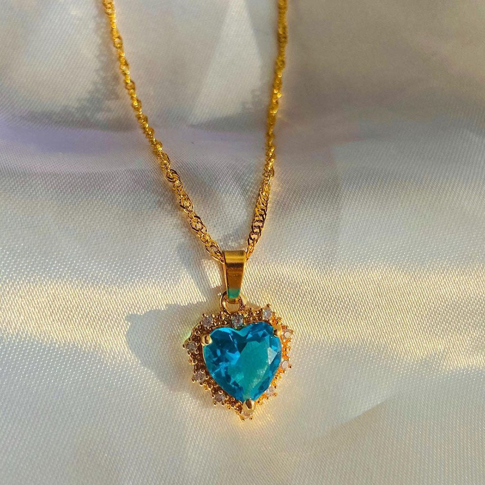 Gold necklace with a heart-shaped turquoise pendant on a white fabric background