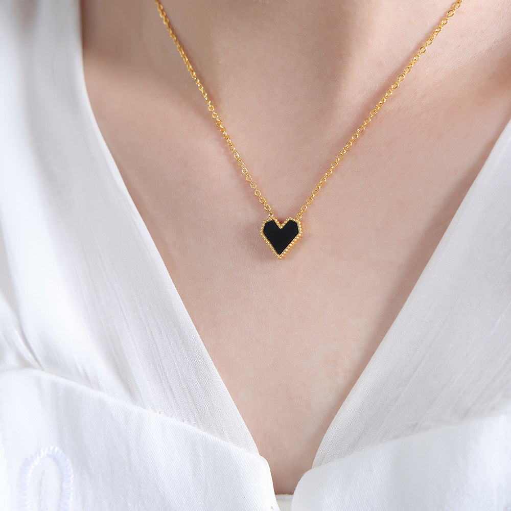 Gold necklace with a black heart pendant worn by a person in a white top.