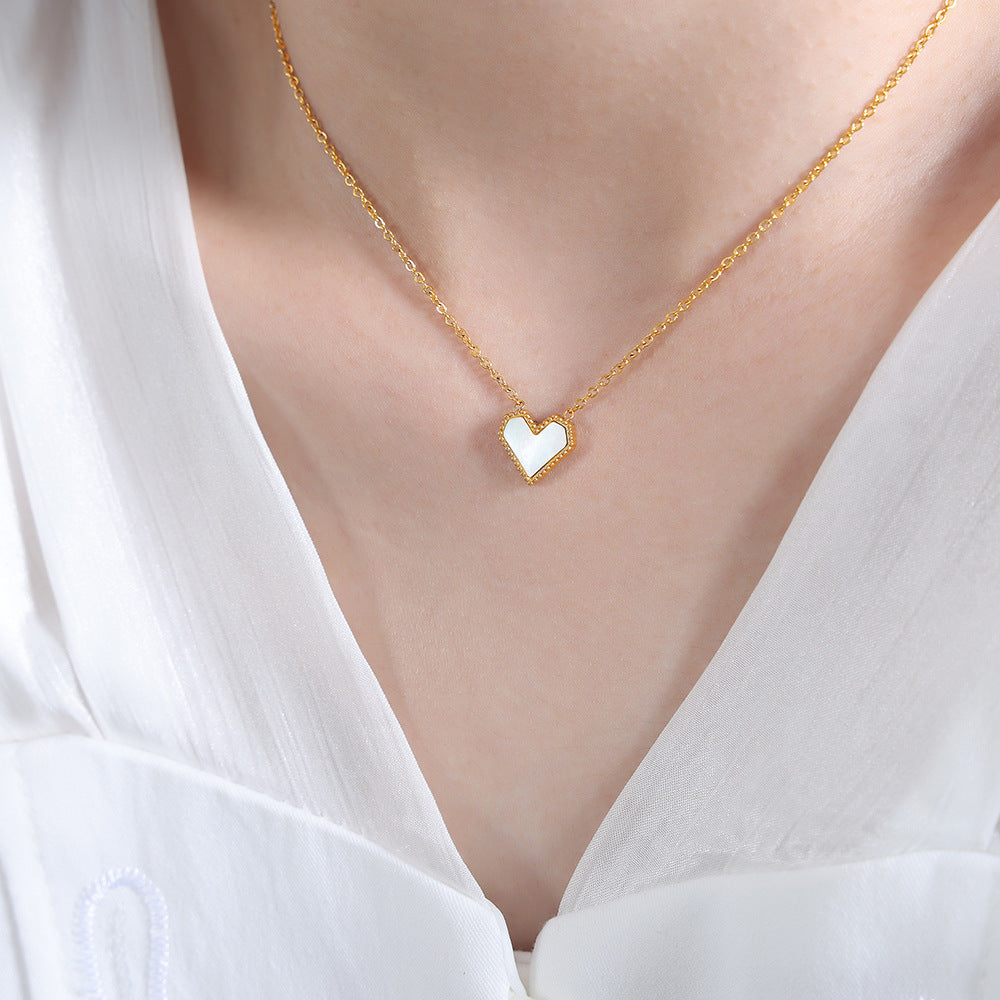 Gold necklace with a heart-shaped pendant worn by a person in a white blouse.