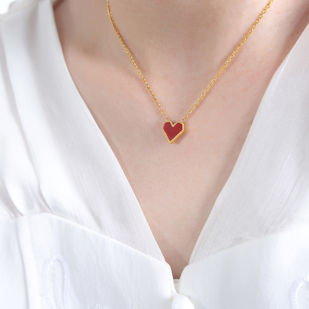 Gold necklace with a red heart pendant on a white background
