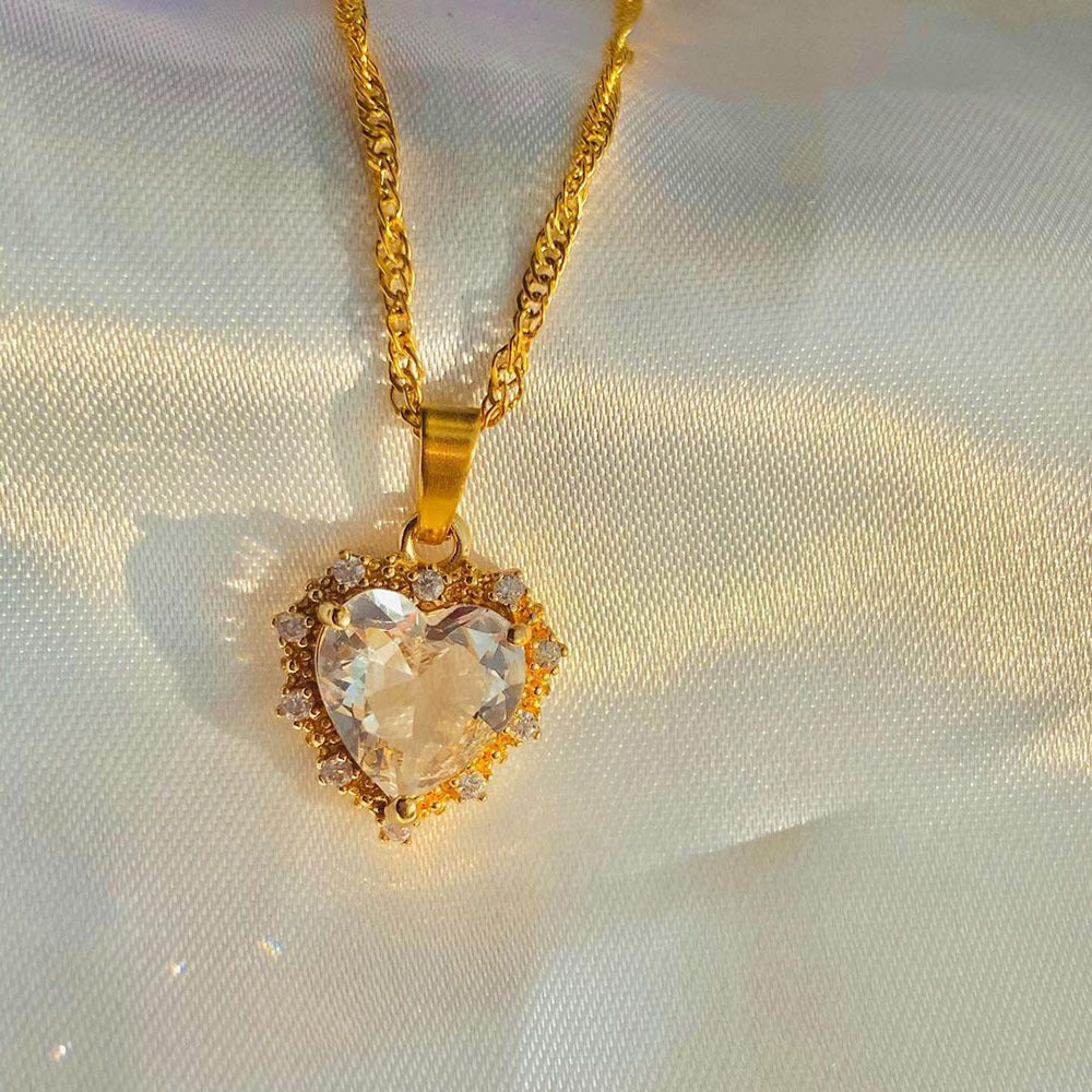 Gold necklace with a heart-shaped pendant on a light fabric background