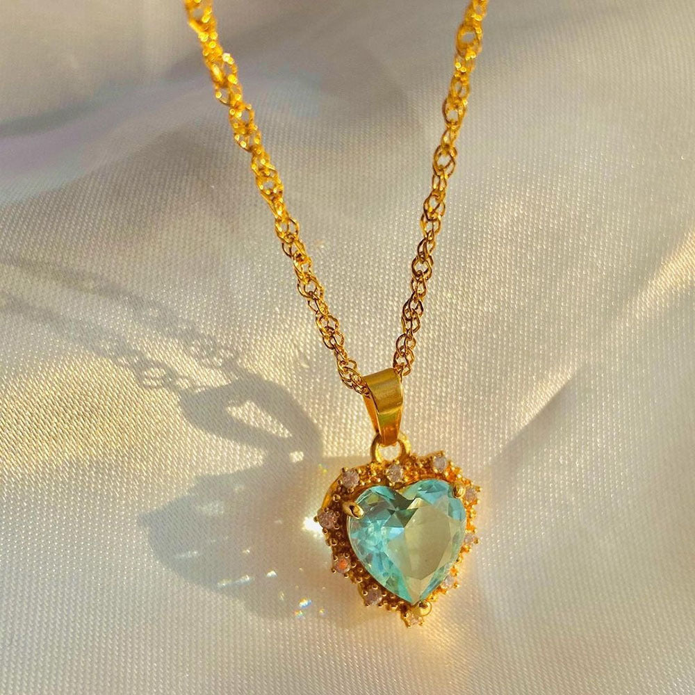 Gold necklace with a heart-shaped turquoise pendant on a light fabric background