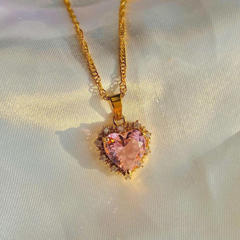 Heart-shaped pink gemstone pendant on a gold chain against a light fabric background