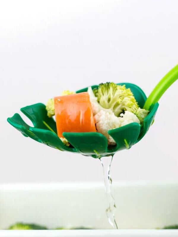 Green kitchen tool with vegetables being rinsed under water