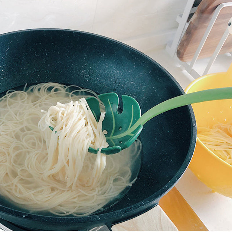 Noodles being lifted from a pot with a green leaf-shaped strainer.