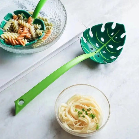 Green leaf-shaped ladle with pasta and a bowl of noodles on a marble surface