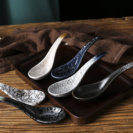 Set of speckled ceramic spoons on a wooden tray with a brown cloth background