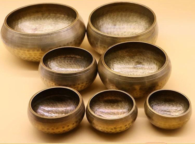 Handmade-Nepalese-singing-bowl-for-chakra Set of bronze bowls with textured interior on a beige background