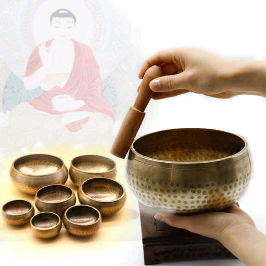 Tibetan singing bowls with a hand holding a mallet, blurred Buddha statue in the background