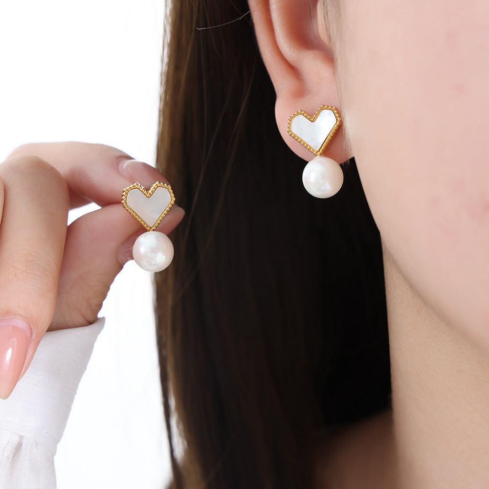 Heart-shaped earrings with pearl drops worn by a person on a white background