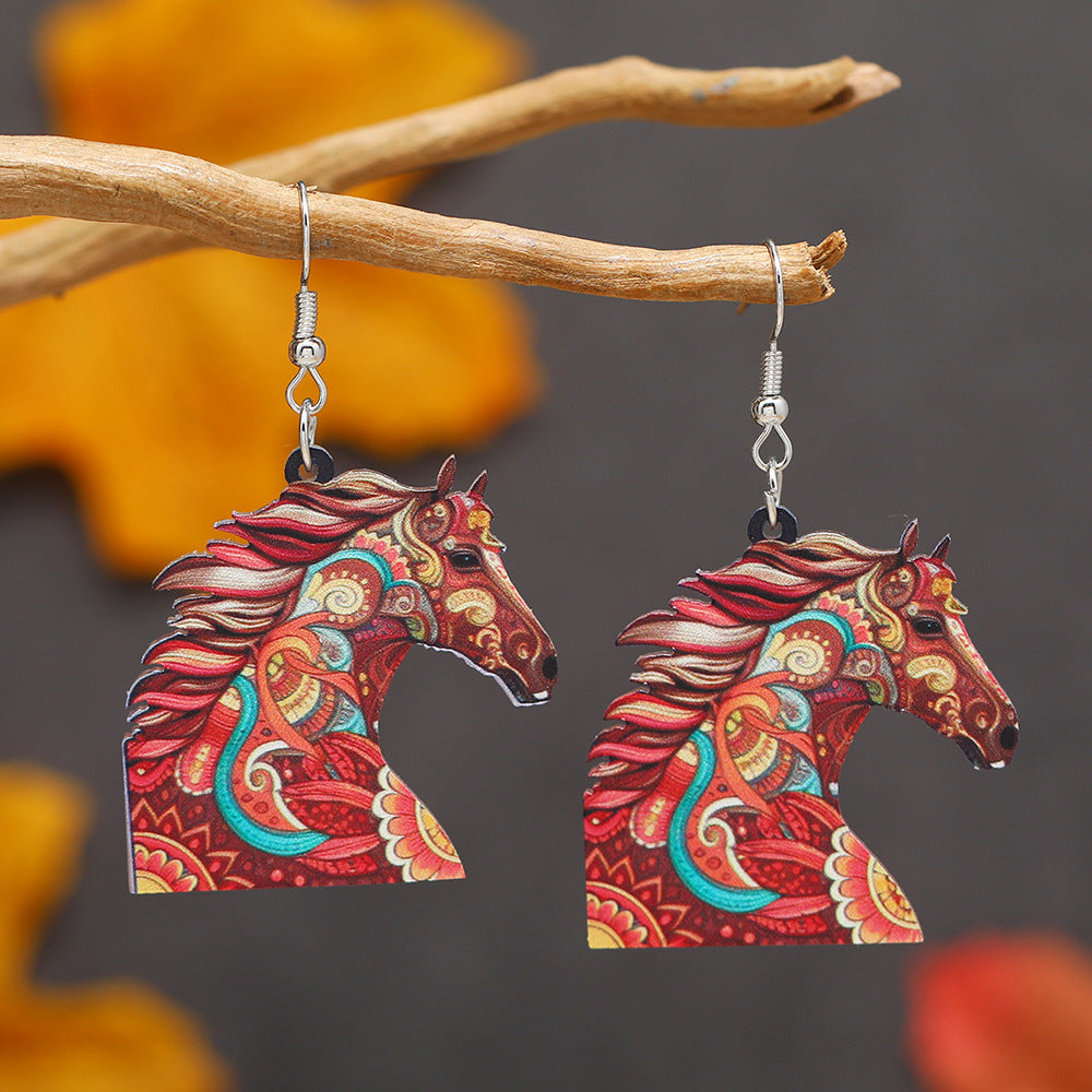 Colorful horse-shaped earrings hanging on a branch with a blurred natural background